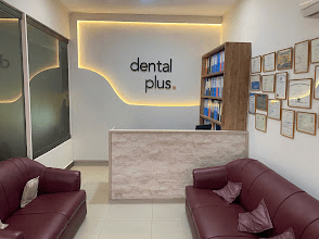 The Dental Plus reception: the clinic logo on a lit wall, a reception desk, framed certificates and two sofas